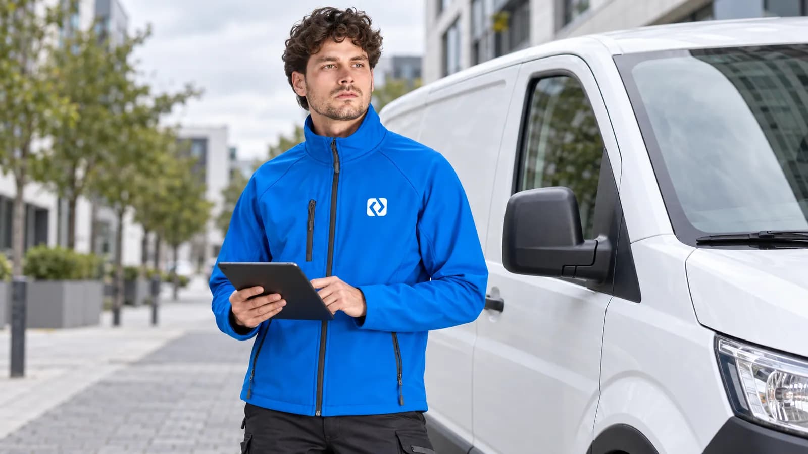 Servicetechniker in blauer Softshelljacke mit Brustlogo neben einem Lieferwagen